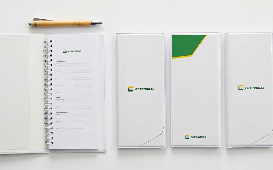 Fotografia de mesa com Tally Books brancos da Petrobras e uma caneta de bambu, demonstrando materiais de anotação para o setor offshore.